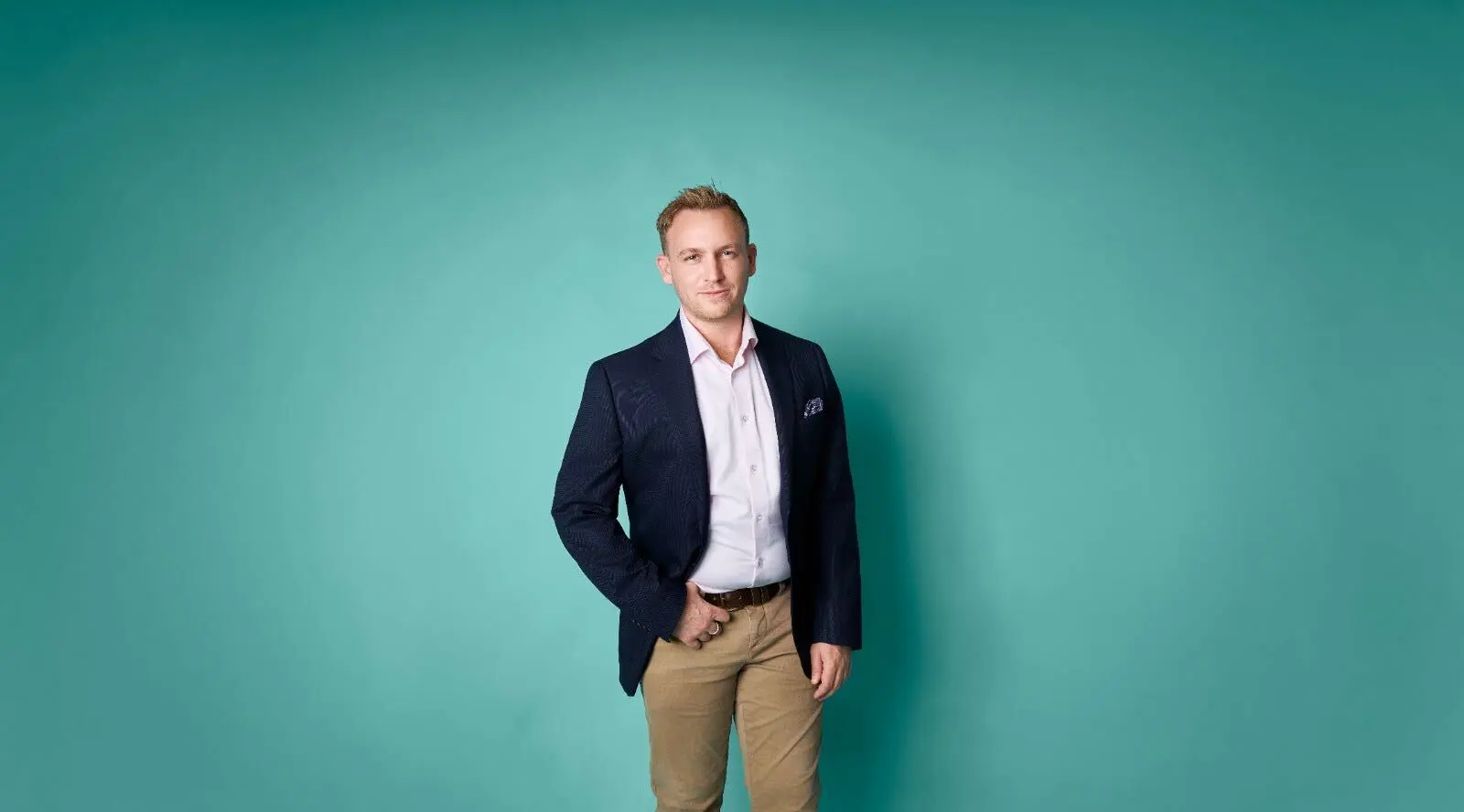 Businessman in a navy blazer and white shirt standing against a teal background